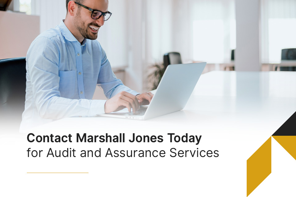 a man is typing on a laptop with the words contact marshall jones today for audit and assurance services