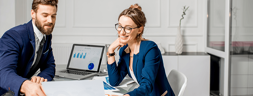 a man and a woman are looking at a laptop with financial data on it