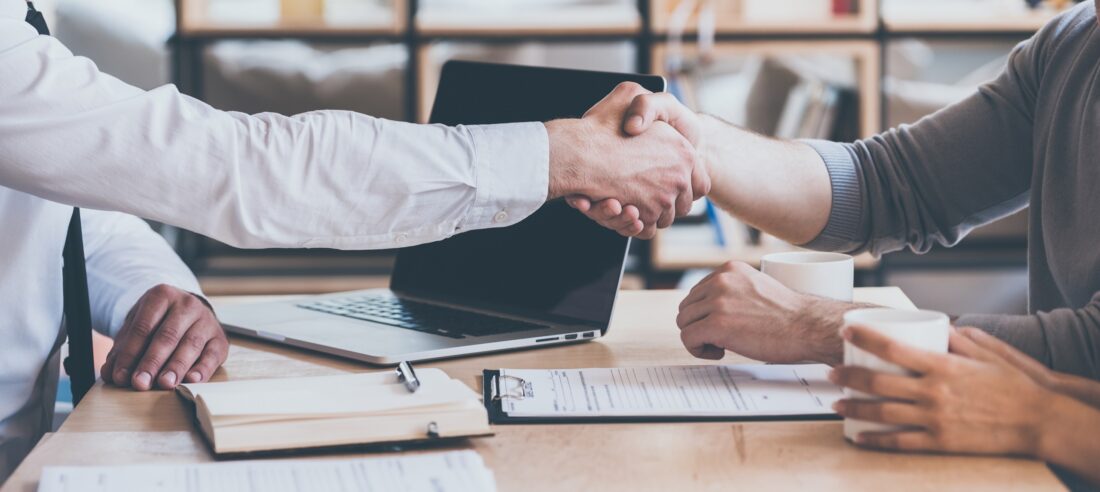 a man shaking hands with another man in front of a laptop