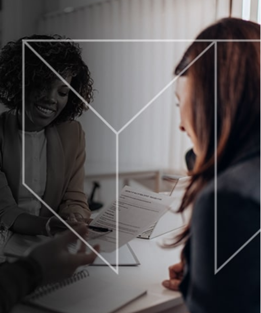 two women are sitting at a table looking at a resume