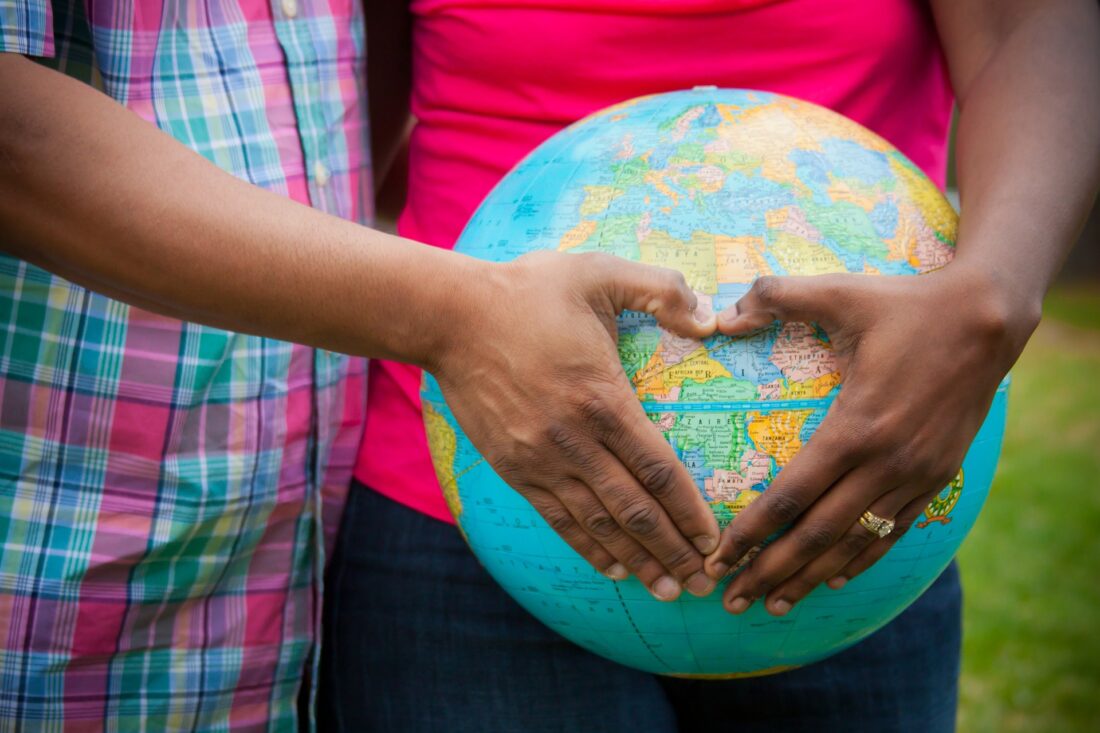 a couple holding a globe with their hands in the shape of a heart