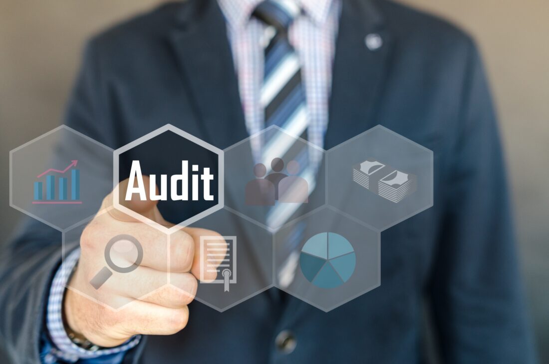 a man in a suit and tie pointing at a screen that says audit