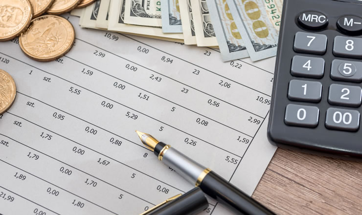 close-up of a pen resting on a financial paper next to coins, dollar bills and a calculator