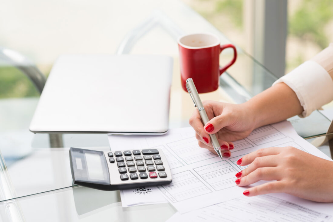 a woman with red nails using a calculator and writing down numbers