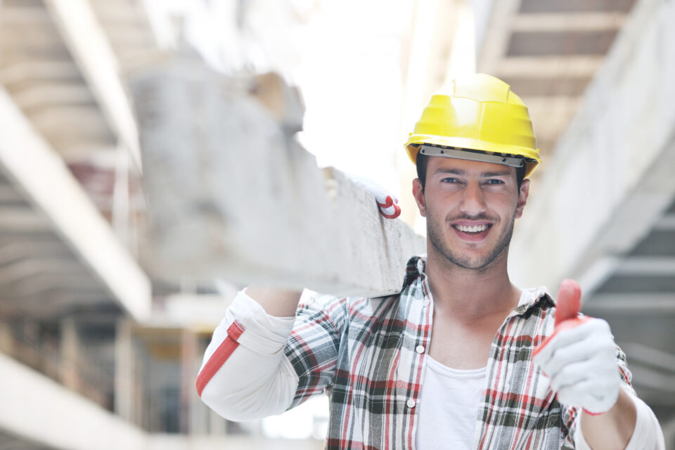 a man wearing a hard hat holding a brick and giving a thumbs up