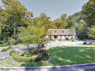 street view of a house with a long driveway and trees surrounding the yard