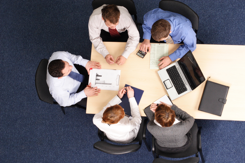 birds' eye view of a group of people sitting around a table with a laptop and a calculator