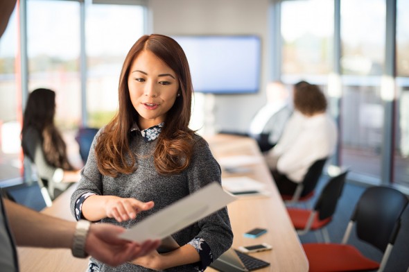 a woman is holding a piece of paper and pointing at it in a conference room