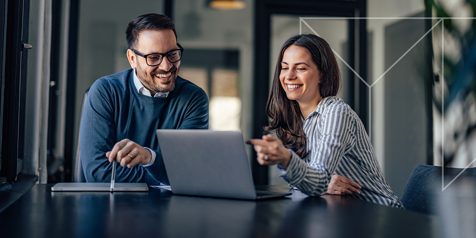 a man and a woman are smiling while looking at a laptop discussing financial tax audits