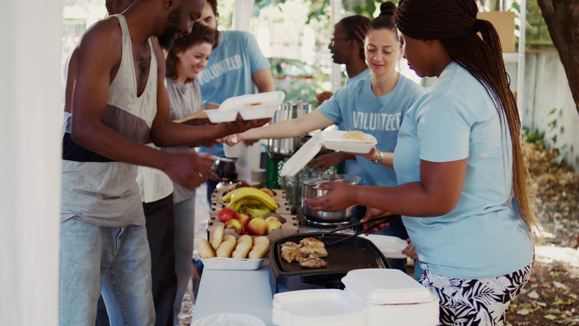 a woman in a blue volunteer shirt serves food to a group of people